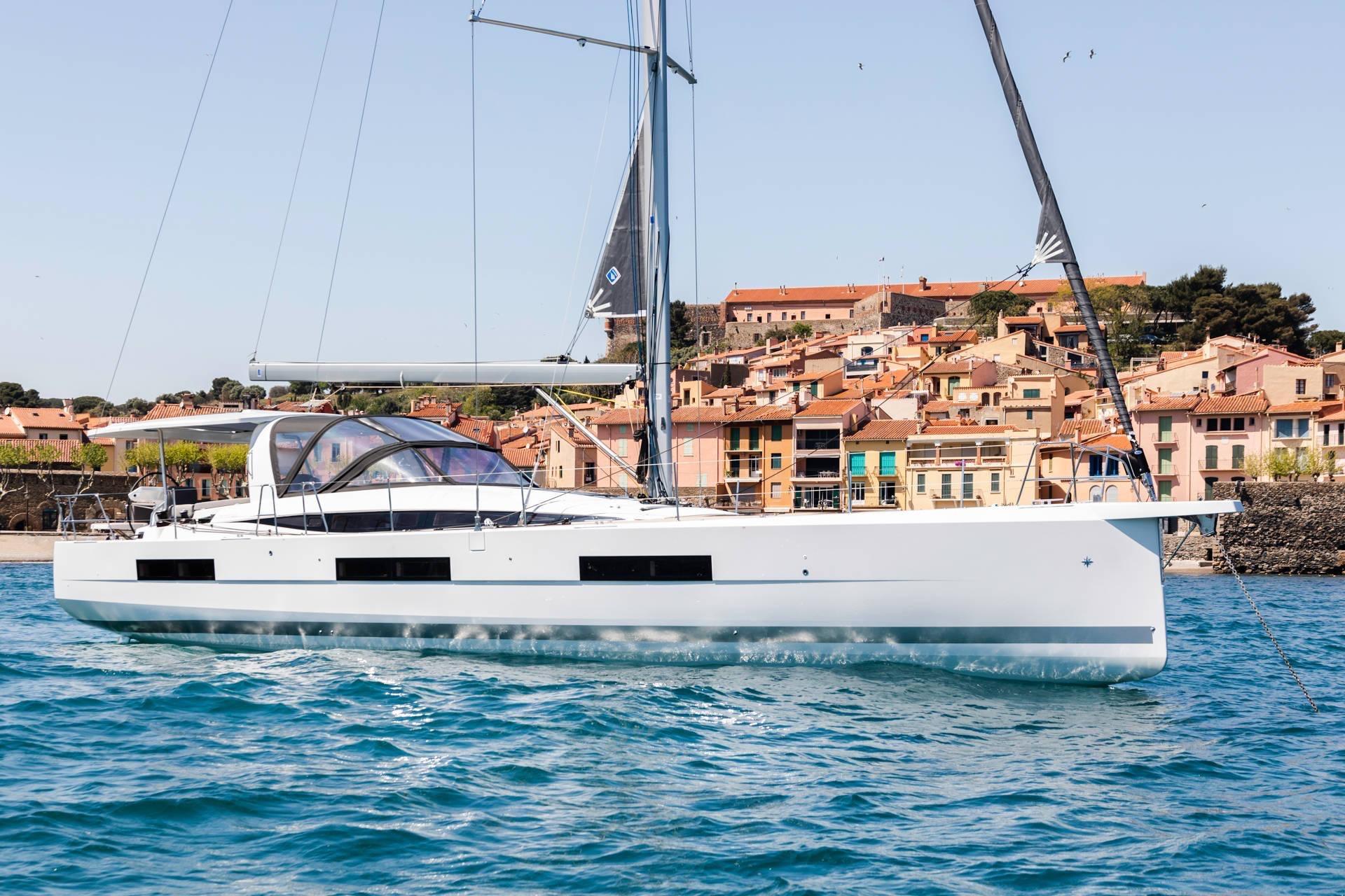 Jeanneau 60 2022 Jeanneau 60 yacht sailing near colorful coastal town.