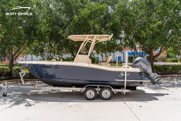 Scout 215 XSF 2023 Scout 215 XSF boat on trailer, parked outdoors with trees in background.