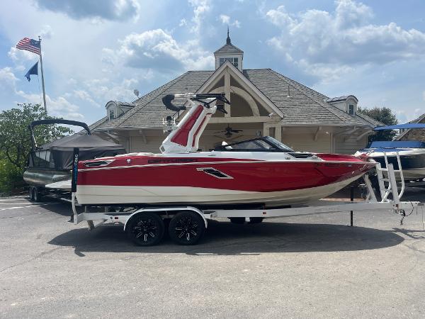 Centurion Ri230 2022 Centurion Ri230 boat in red and white on a trailer, parked outside a building.