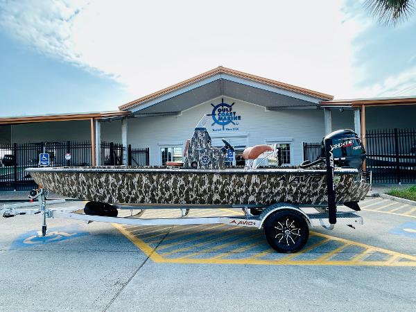 Avid 21 FST GCE 2025 Avid 21 FST GCE boat with camouflage design on a trailer, parked outside a building.