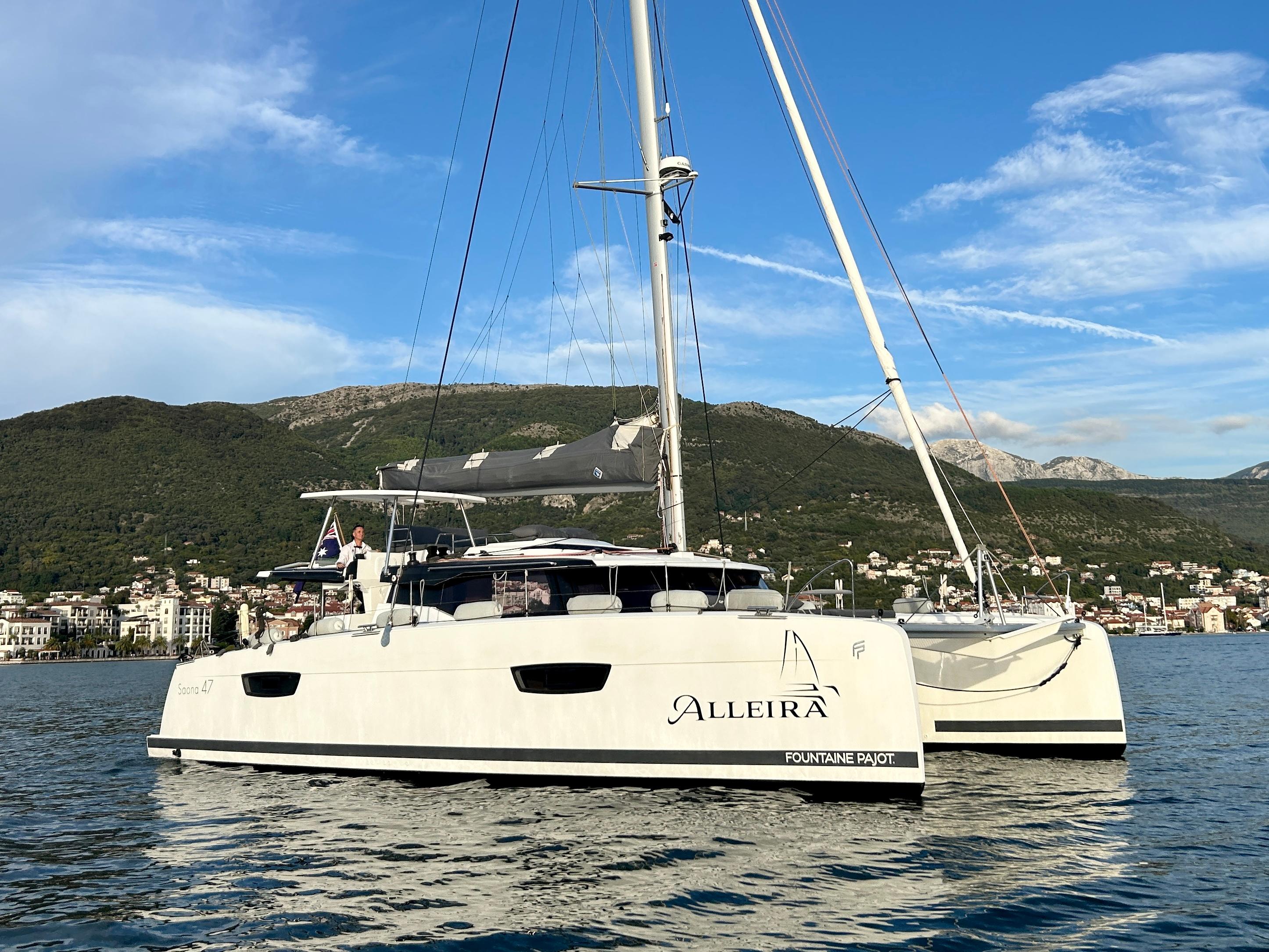 Fountaine Pajot Saona 47 2021 Fountaine Pajot Saona 47 catamaran sailing near a coastal town with mountains.
