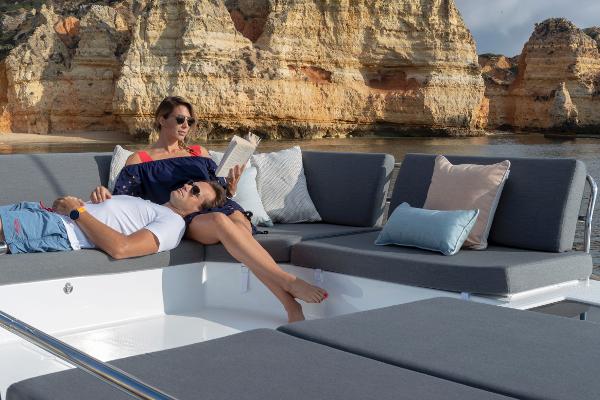 Fountaine Pajot Elba 45 Couple relaxing on 2024 Fountaine Pajot Elba 45 catamaran with scenic cliff backdrop.