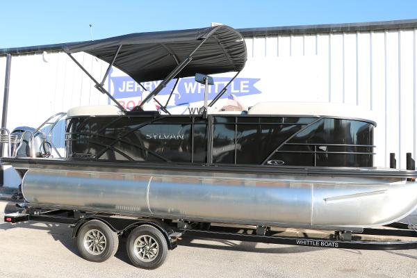 Sylvan Mirage X1 2025 Sylvan Mirage X1 pontoon boat on trailer, black canopy, parked outside.