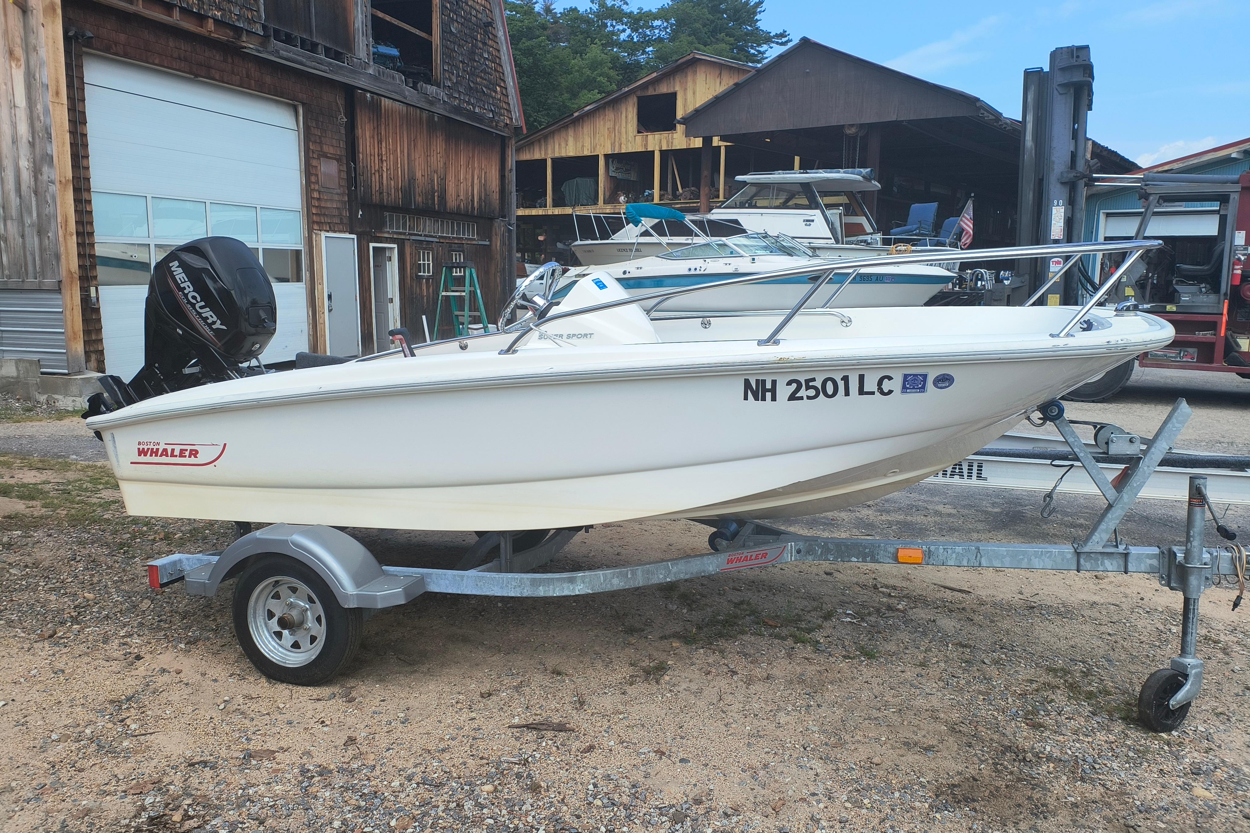 Boston Whaler 130 Super Sport 2016 Boston Whaler 130 Super Sport boat on trailer, parked near rustic buildings.