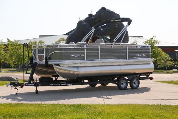 Sun Tracker Fishin' Barge 20 DLX 2025 Sun Tracker Fishin' Barge 20 DLX pontoon boat on a trailer in a parking lot.