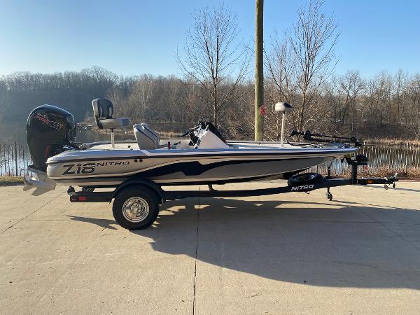 Nitro Z18 2025 Nitro Z18 boat on trailer, parked near a lake with trees in the background.
