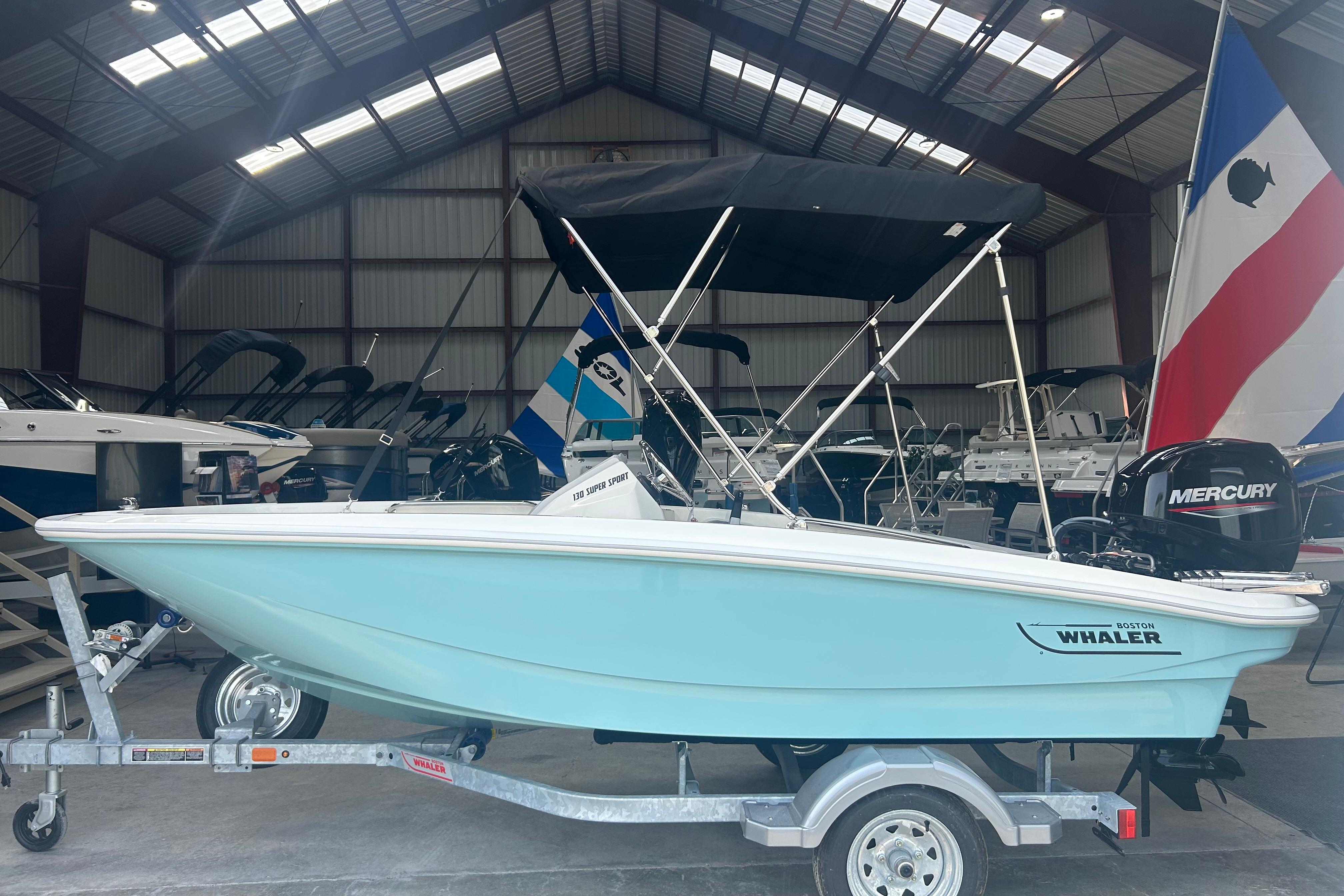 Boston Whaler 130 Super Sport 2025 Boston Whaler 130 Super Sport boat in a showroom, featuring a Mercury engine.