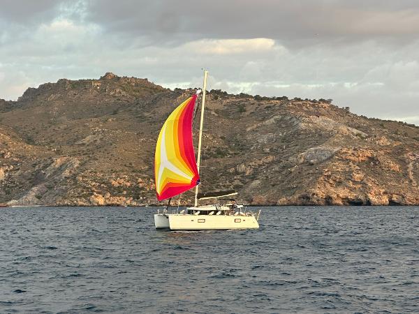 Lagoon 400 Sailing catamaran Lagoon 400 (2012) with colorful spinnaker near rocky coastline.