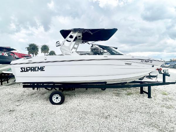 Supreme S220 2023 Supreme S220 boat on trailer, white exterior, black canopy, parked outdoors.