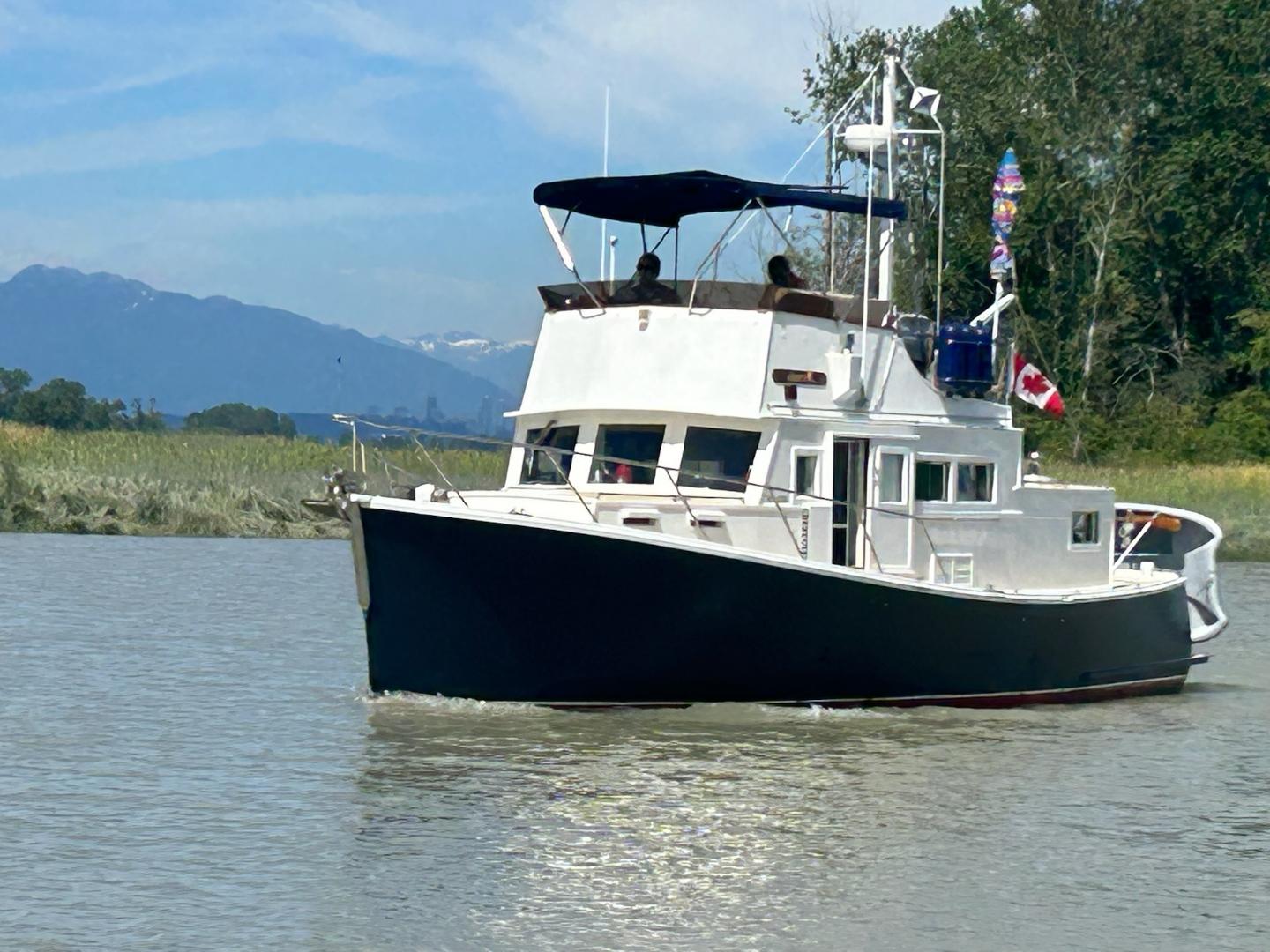 Custom Tri-Cabin 1970 Custom Tri-Cabin boat cruising on a scenic river with mountains in the background.