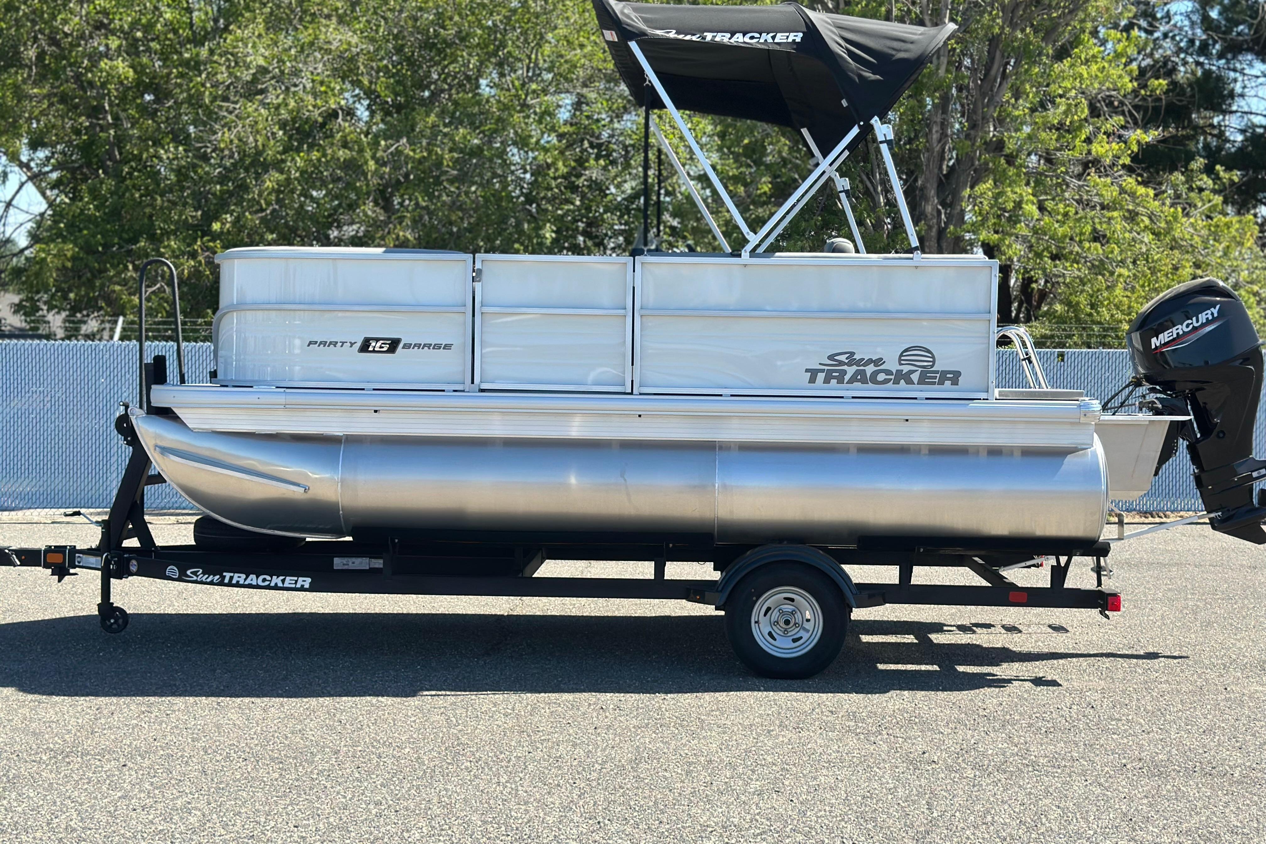 Sun Tracker Party Barge 16 DLX 2026 Sun Tracker Party Barge 16 DLX pontoon boat on trailer, parked outdoors.