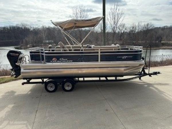 Sun Tracker Fishin' Barge 20 DLX 2025 Sun Tracker Fishin' Barge 20 DLX pontoon boat on trailer by a lake.
