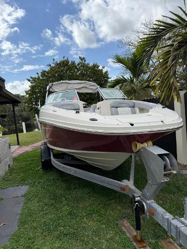 Sea Ray 220 Sundeck 2010 Sea Ray 220 Sundeck boat on trailer, parked on grass, with palm trees and cloudy sky.