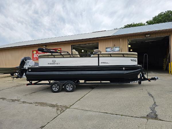 Regency 230 DL3 2024 Regency 230 DL3 pontoon boat on a trailer outside a warehouse.