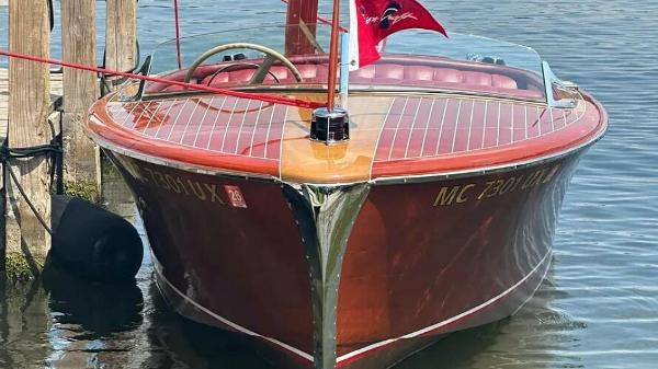 Chris-Craft Riviera 1951 Chris-Craft Riviera boat docked, showcasing classic wooden design and red flag.