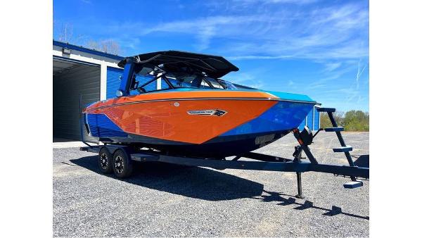 Nautique Super Air Nautique G23 2024 Nautique Super Air Nautique G23 boat in vibrant orange and blue, parked on a trailer.