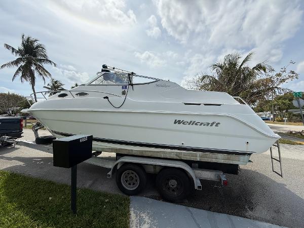 Wellcraft 2400 Martinique 2000 Wellcraft 2400 Martinique boat on trailer, parked near palm trees under cloudy sky.