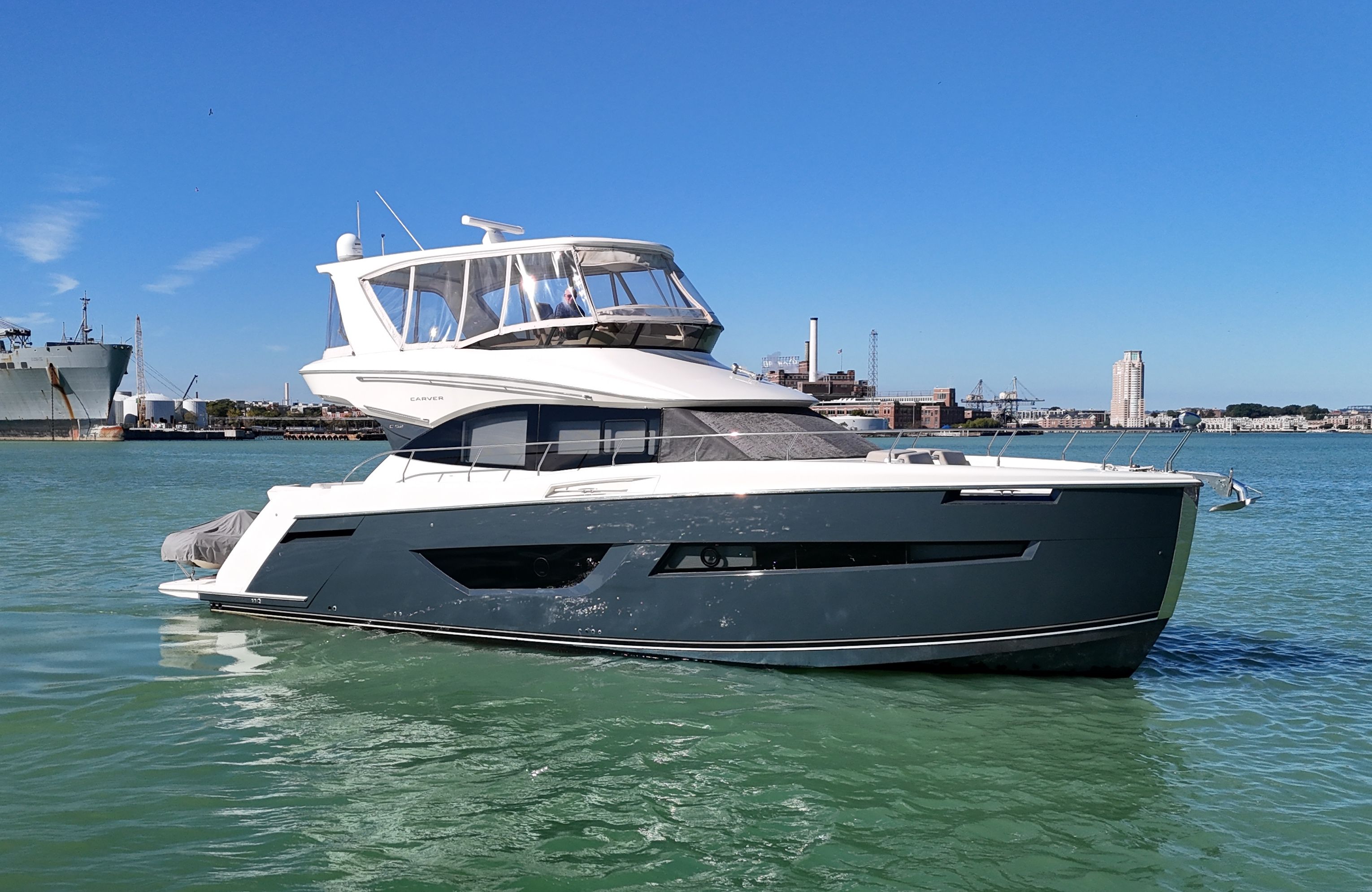 Carver C52 Flybridge 2018 Carver C52 Flybridge yacht on calm water with cityscape background.