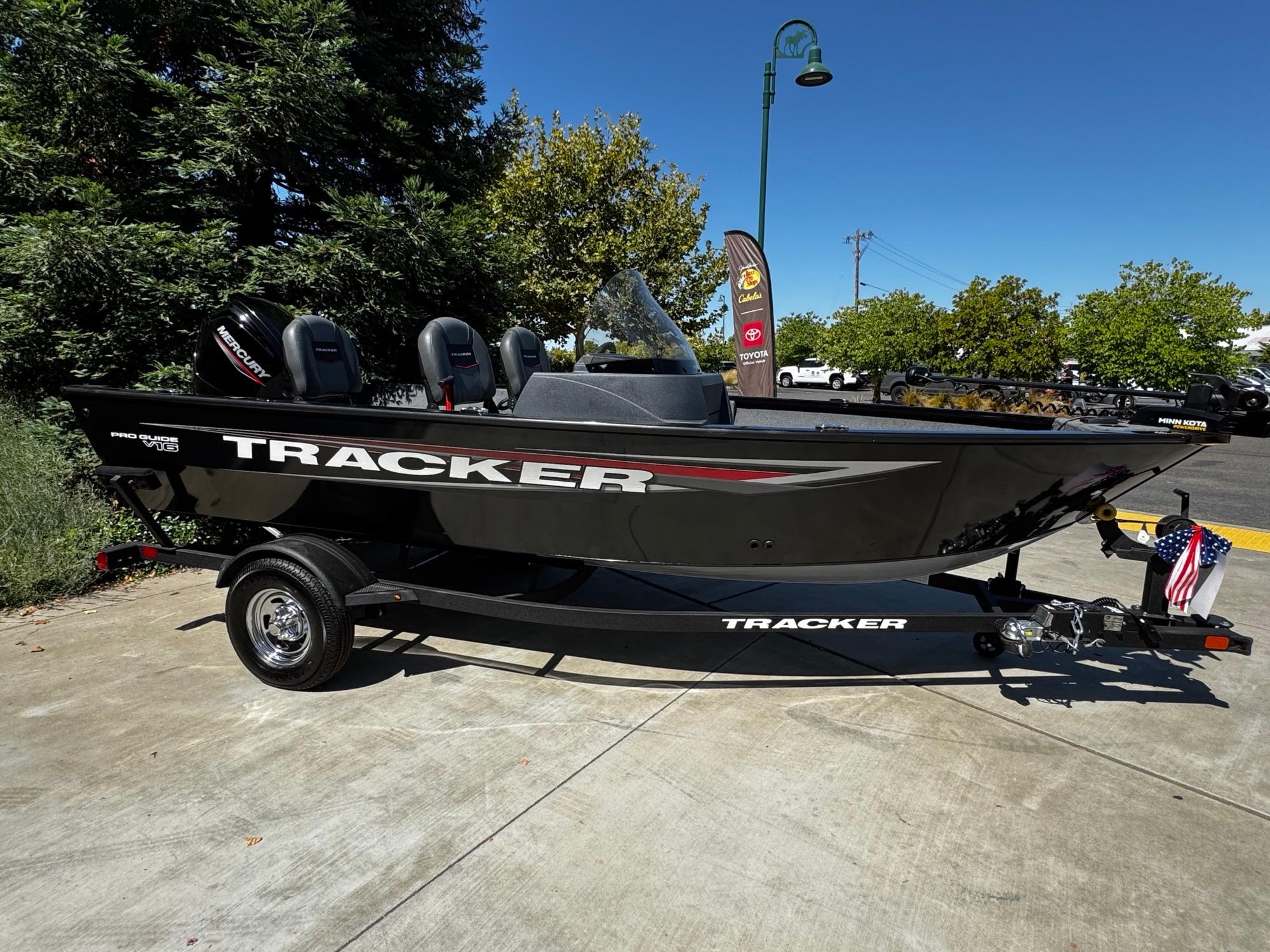 Tracker Pro Guide V-16 SC 2025 Tracker Pro Guide V-16 SC boat on trailer, parked outdoors, with trees and clear sky.