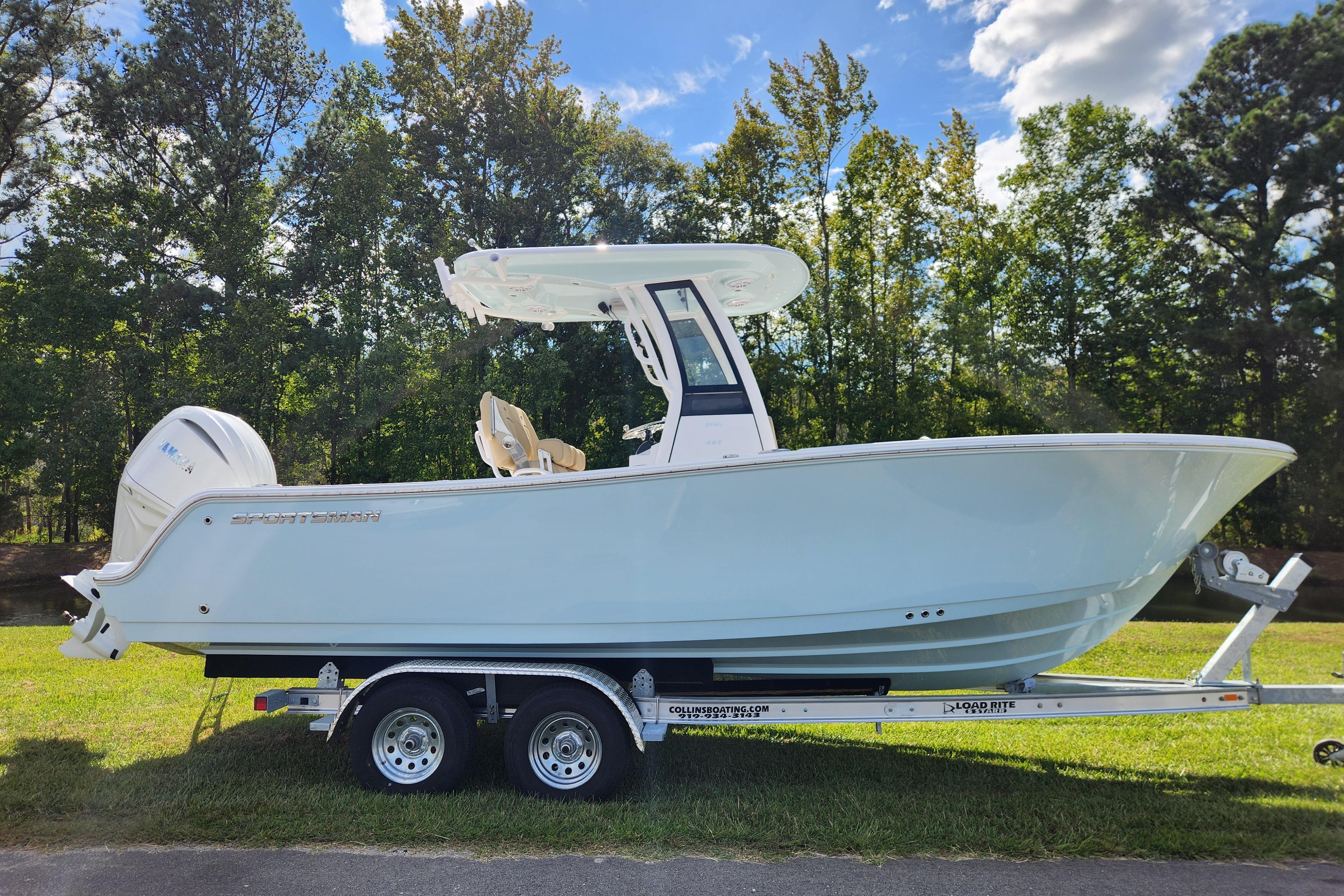 Sportsman Open 232 Center Console 2026 Sportsman Open 232 Center Console boat on trailer, parked on grass with trees in background.