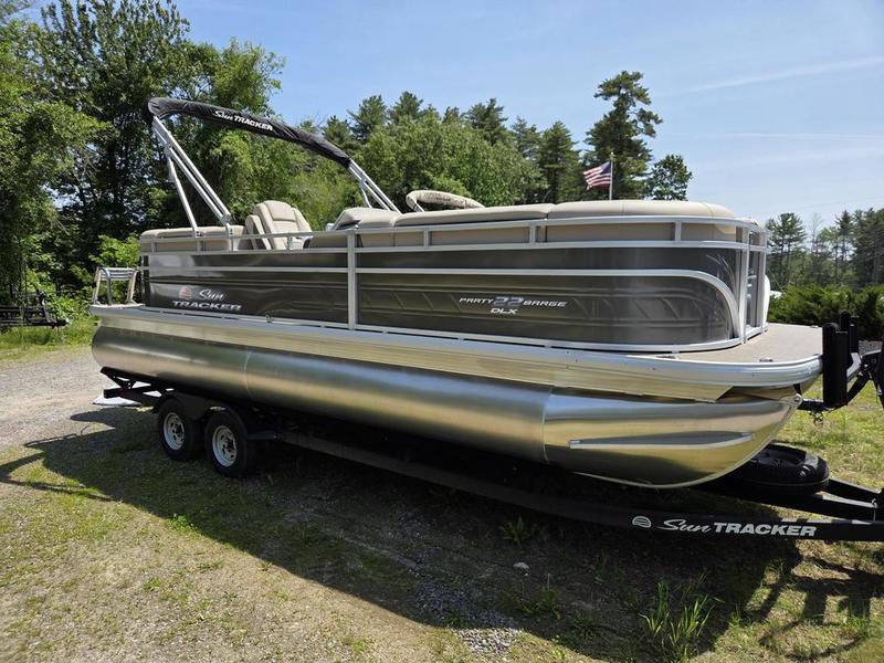 Sun Tracker Party Barge 22 DLX 2025 Sun Tracker PARTY BARGE® 22 DLX pontoon boat on trailer, parked outdoors.