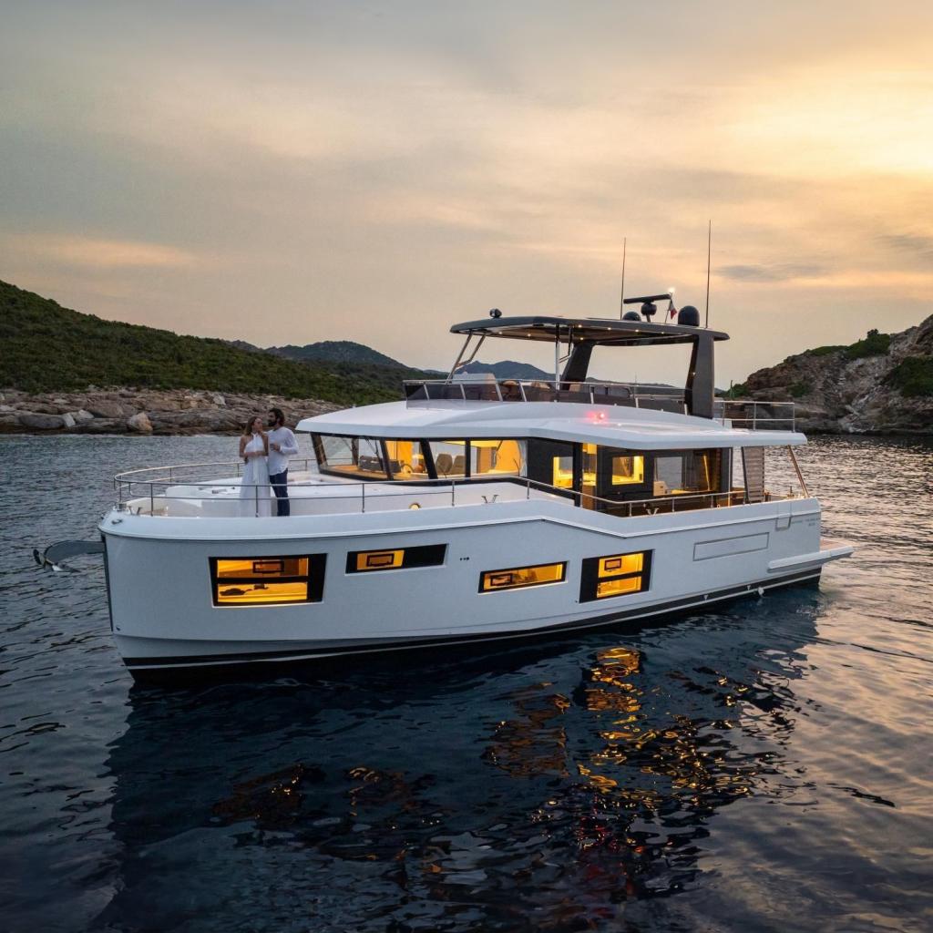 Beneteau Grand Trawler 63 2026 Beneteau Grand Trawler 63 yacht at sunset, with illuminated windows and scenic backdrop.