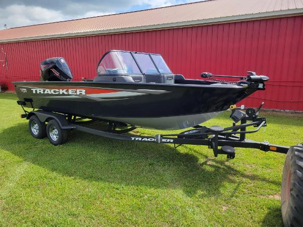 Tracker Targa V-19 WT 2025 Tracker Targa V-19 WT boat on trailer, parked on grass by red building.