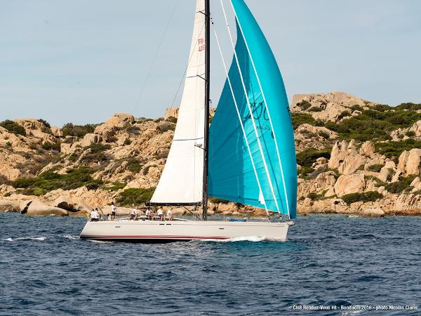 CNB BORDEAUX 60 Sailing yacht CNB BORDEAUX 60, 2009, with blue spinnaker near rocky coastline.