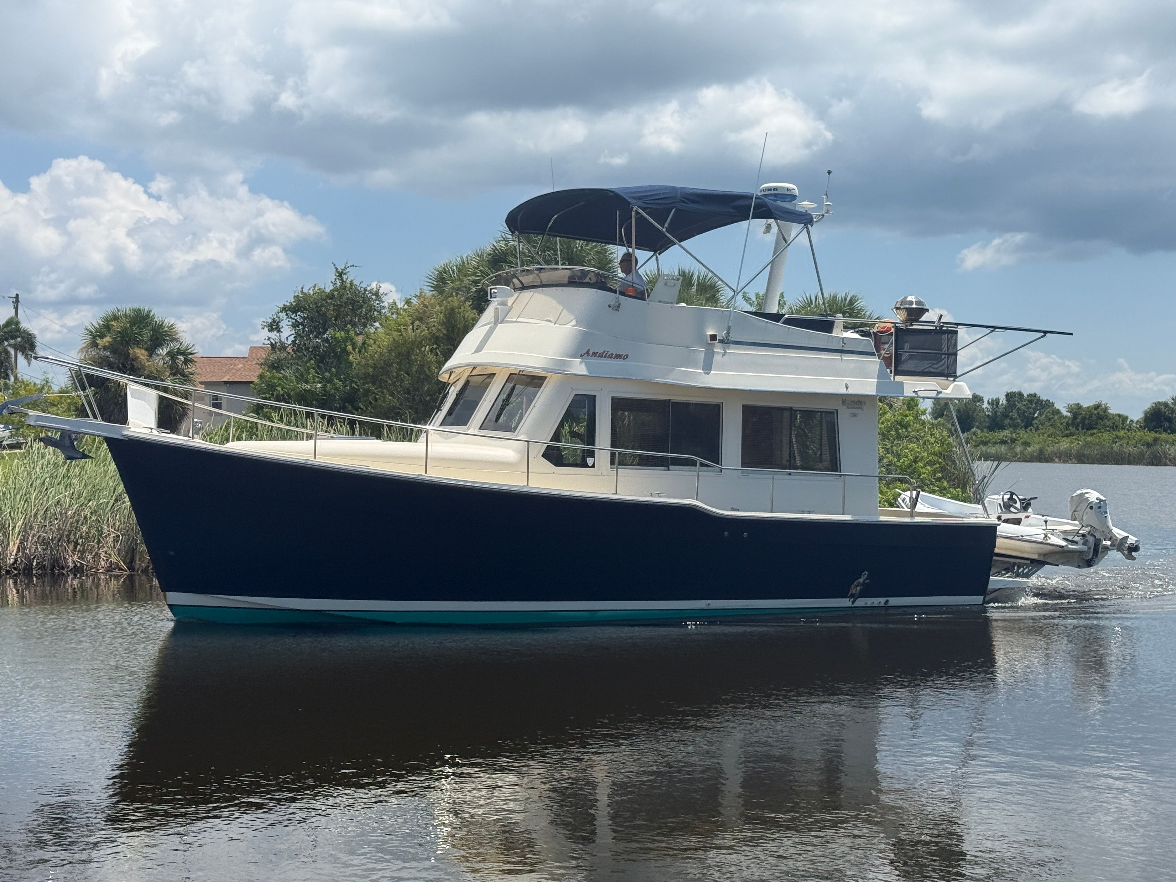Mainship 34 Trawler 2006 Mainship 34 Trawler on calm water, surrounded by lush greenery and cloudy sky.
