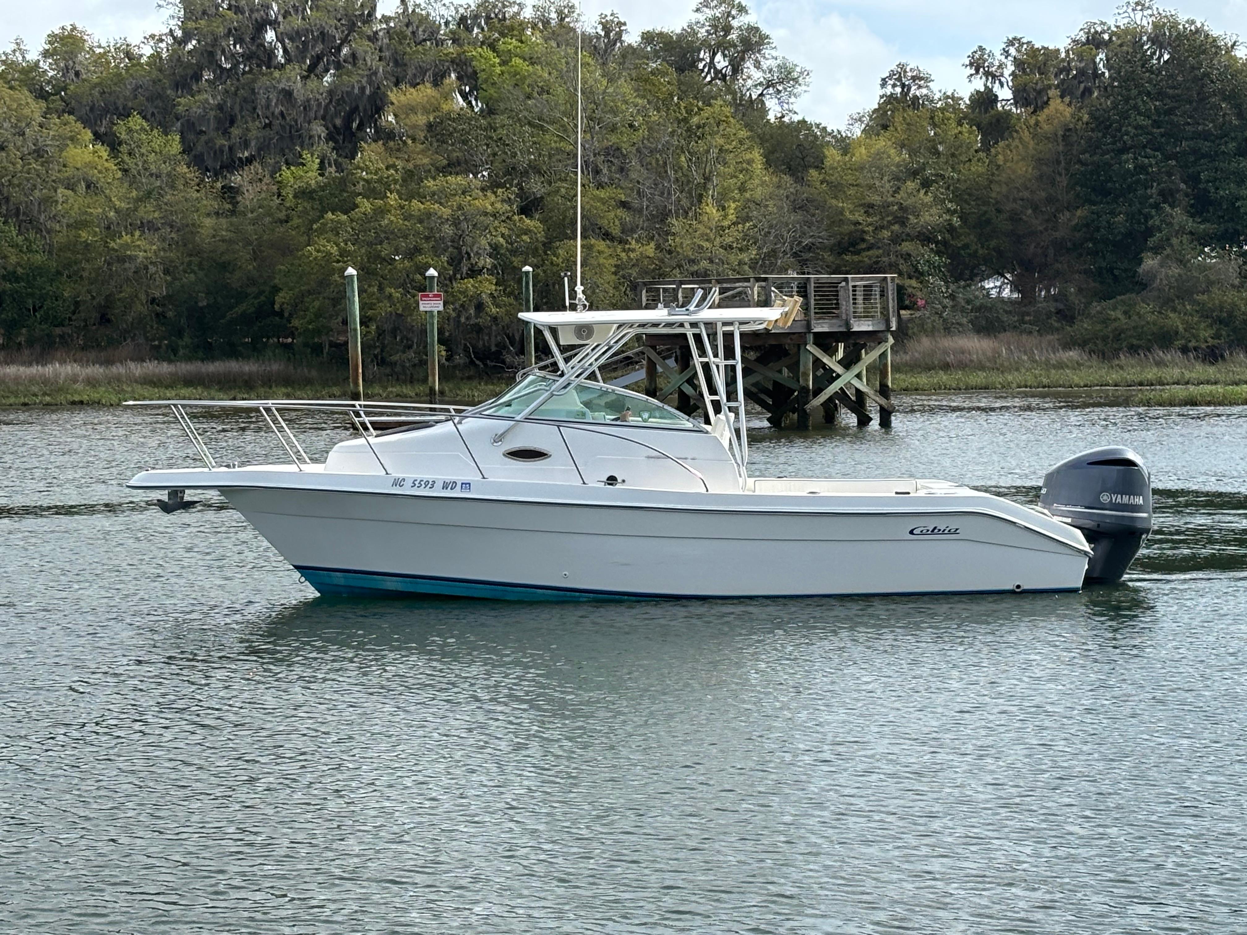 Cobia 230WA 1997 Cobia 230WA boat on calm water near a wooden dock, surrounded by trees.