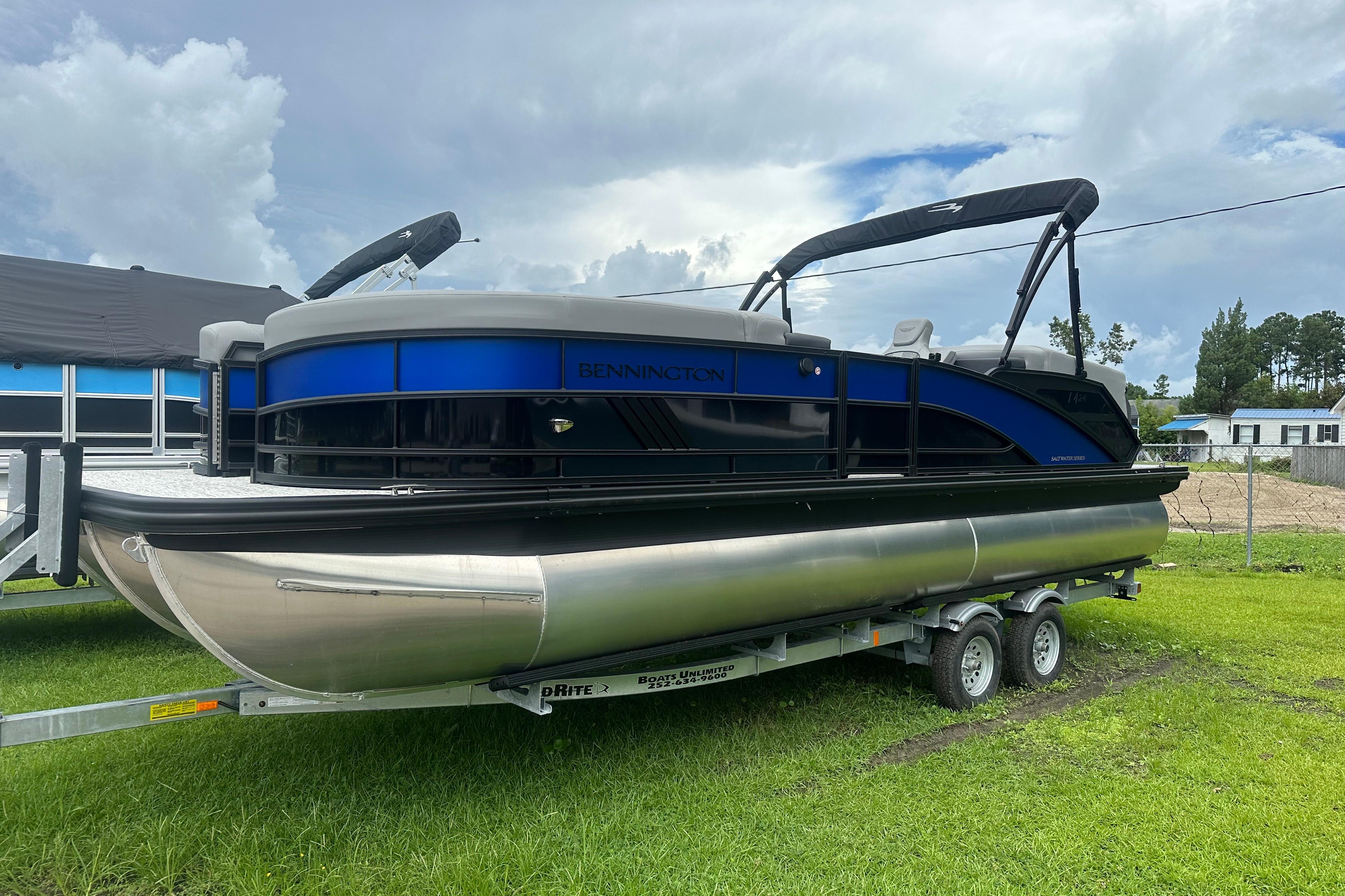 Bennington 24M 2025 Bennington 24M pontoon boat on trailer, parked on grass under cloudy sky.