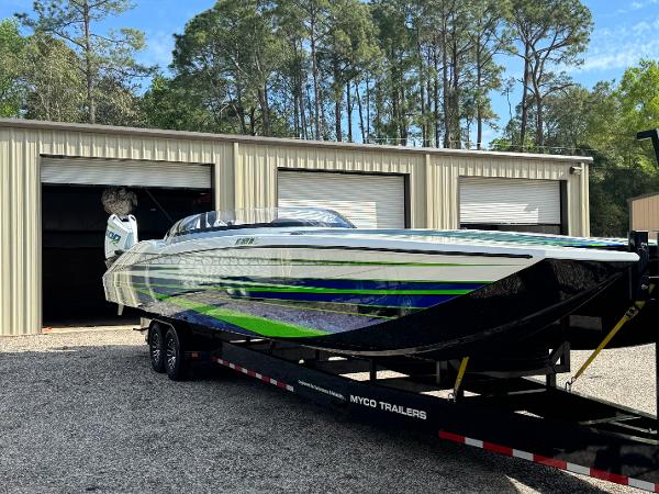 MTI 390X 2023 MTI 390X speedboat on trailer, parked outside a garage with trees in the background.