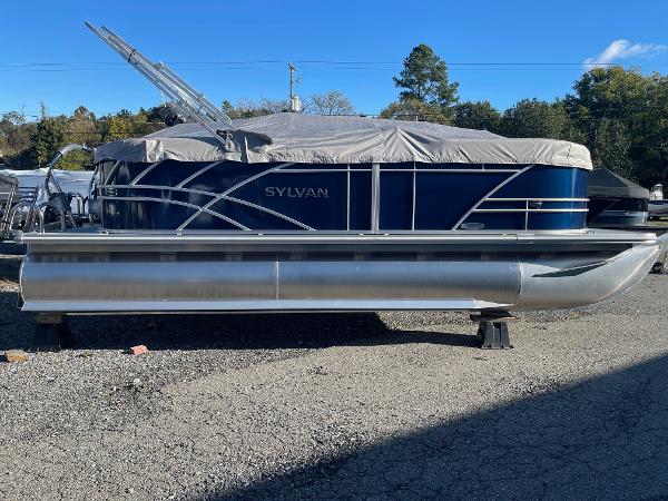 Sylvan 8520 LZ 2025 Sylvan 8520 LZ pontoon boat with cover, parked on gravel lot.