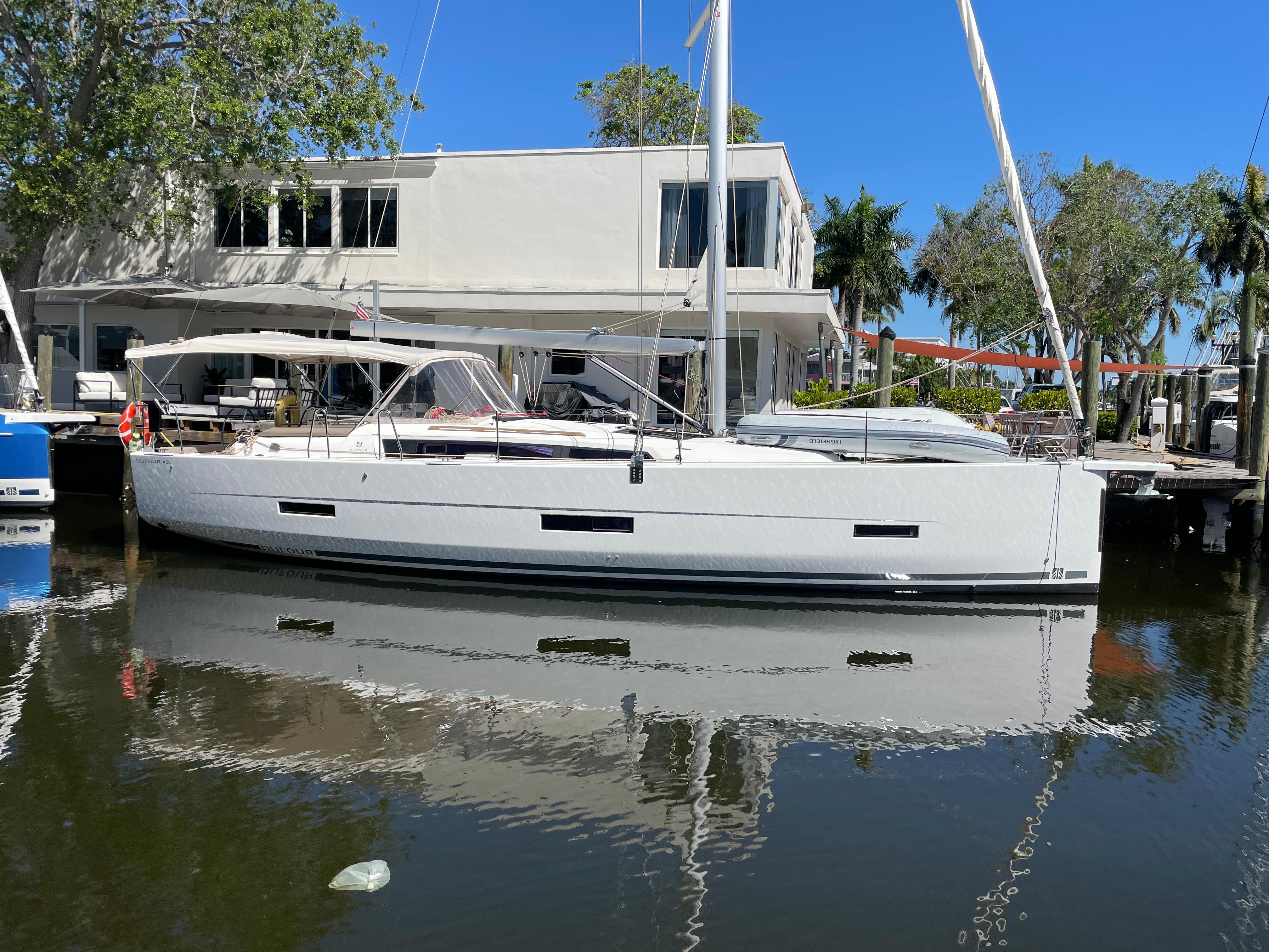Dufour 430 2022 Dufour 430 sailboat docked by modern waterfront home, clear blue sky.
