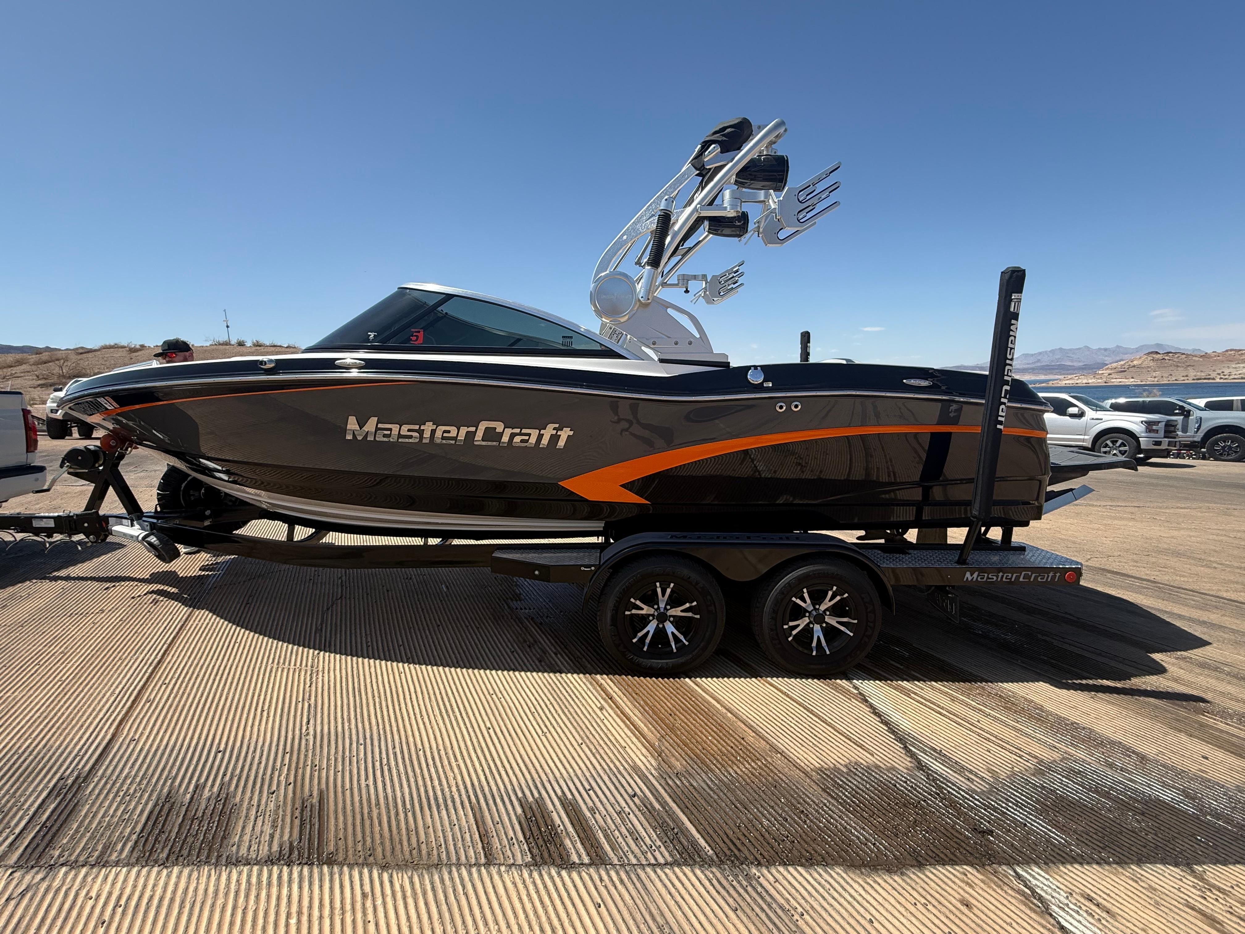MasterCraft X10 2015 MasterCraft X10 boat on trailer, sleek design, black and orange accents, sunny day.
