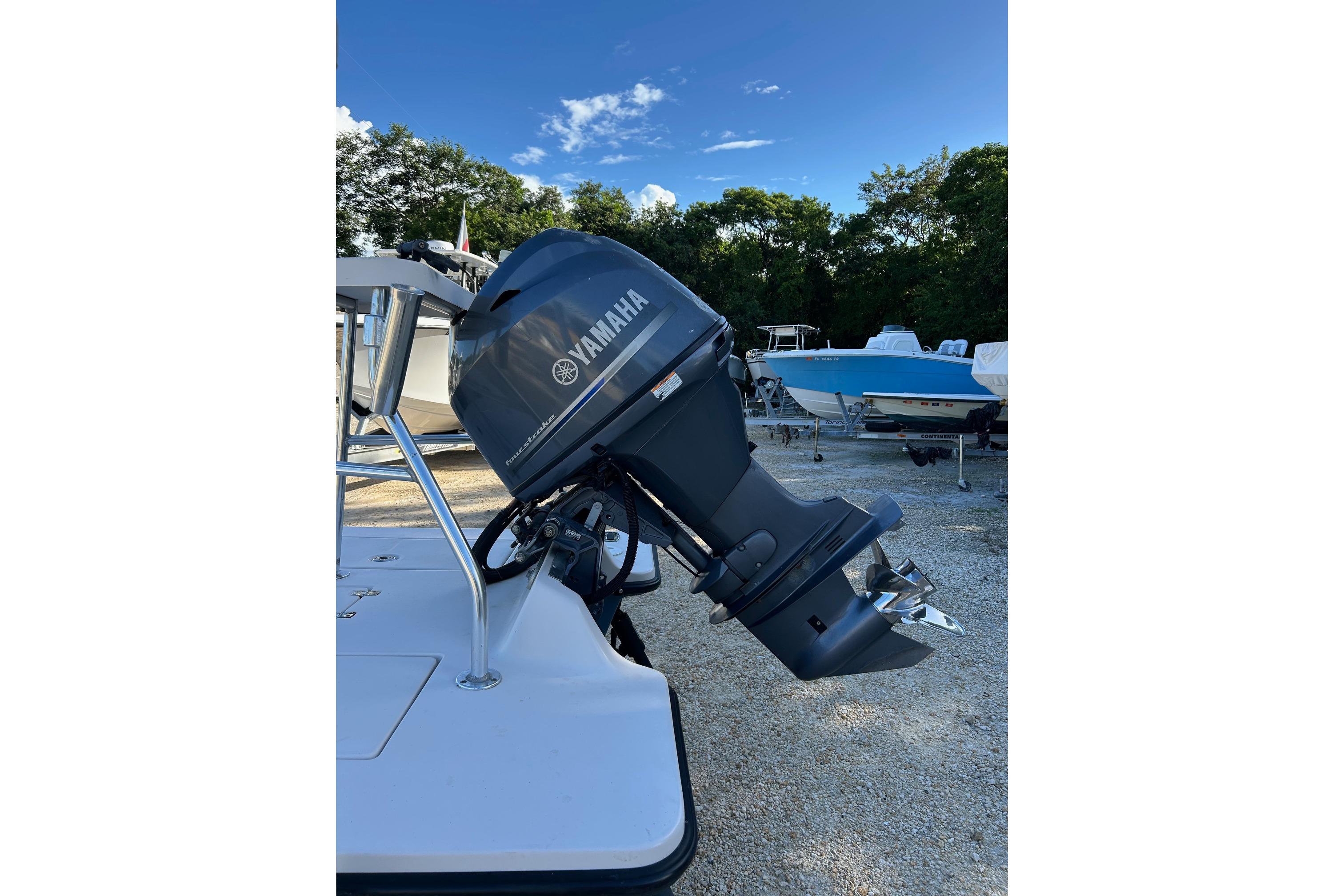 Maverick Hue Outboard motor on a 2005 Tailfisher Hue boat, parked on gravel with trees in background.