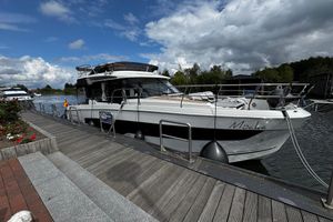 Jeanneau Merry Fisher 1295 Fly 2023 Jeanneau Merry Fischer 1295 docked by a scenic riverside under a partly cloudy sky.