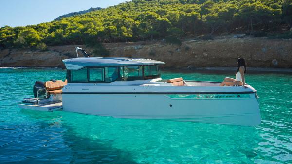 Saxdor 320 GTC Saxdor 320 GTC 2025 model boat in clear turquoise water near a forested coastline.