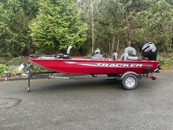 Tracker Pro 170 2025 Tracker Pro 170 boat in vibrant red, parked on a trailer, surrounded by lush greenery.