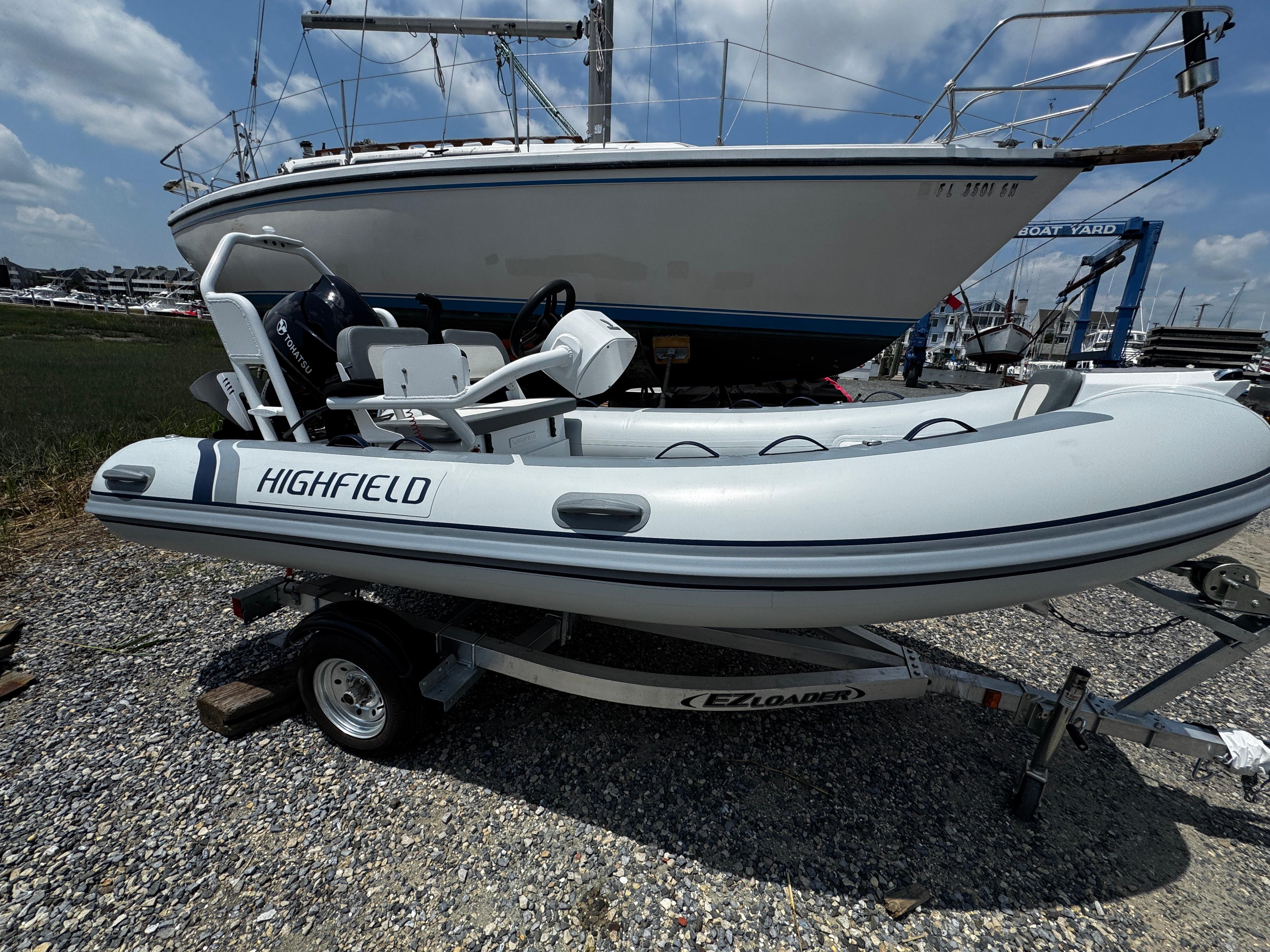 Highfield Classic 400 2025 Highfield Classic 400 inflatable boat on trailer, parked near larger sailboat.