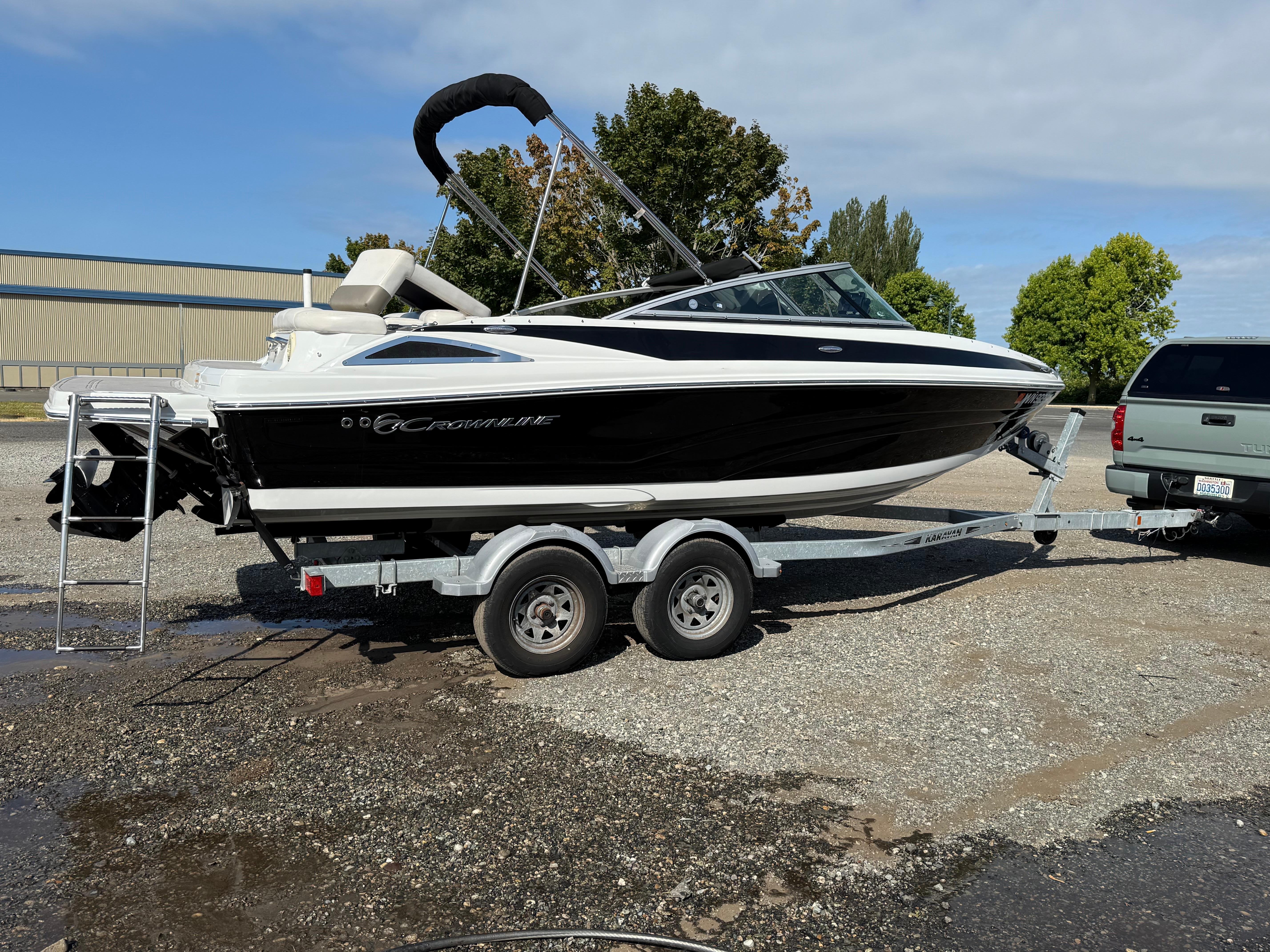 Crownline 205 SS 2017 Crownline 205 SS boat on trailer, parked outdoors, with trees and a building in the background.