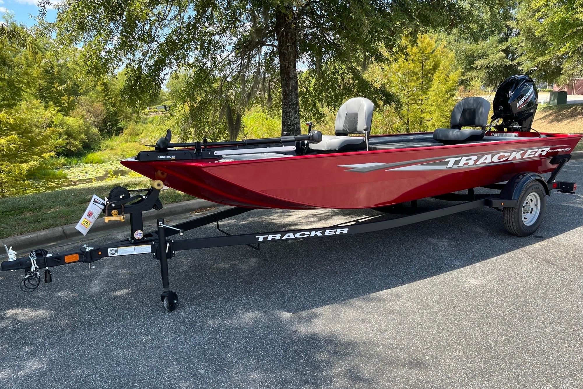 Tracker Panfish 17 2025 Tracker Panfish 17 boat in red, parked on a trailer, surrounded by greenery.
