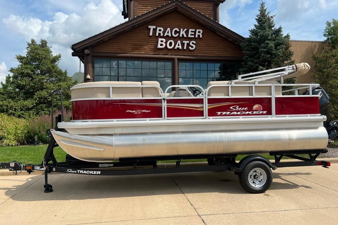 Sun Tracker Party Barge 18 DLX 2025 Sun Tracker Party Barge 18 DLX pontoon boat on trailer outside Tracker Boats store.