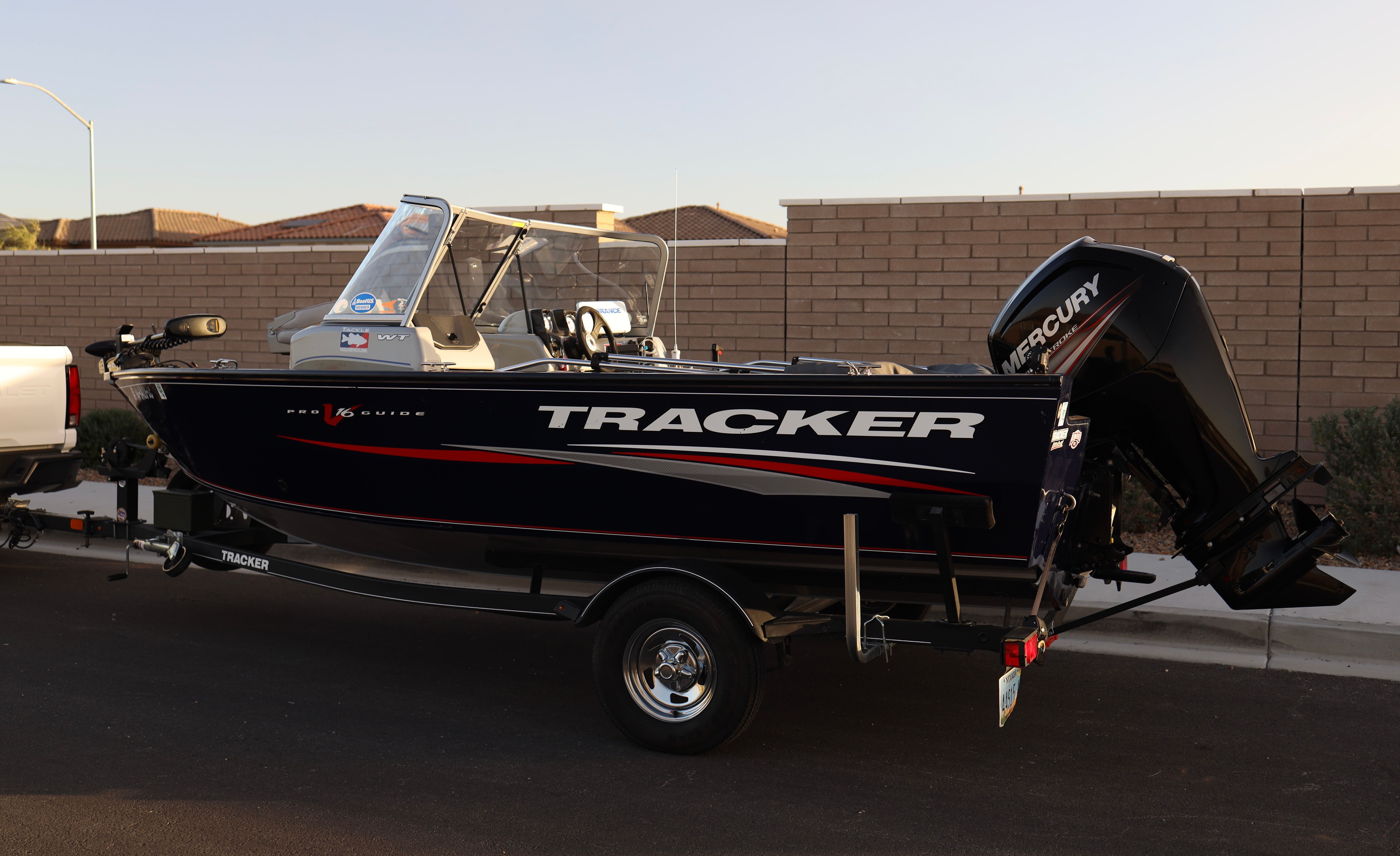 Tracker V16 WT 2019 Tracker V16 WT boat on trailer, parked on street, with Mercury outboard motor.