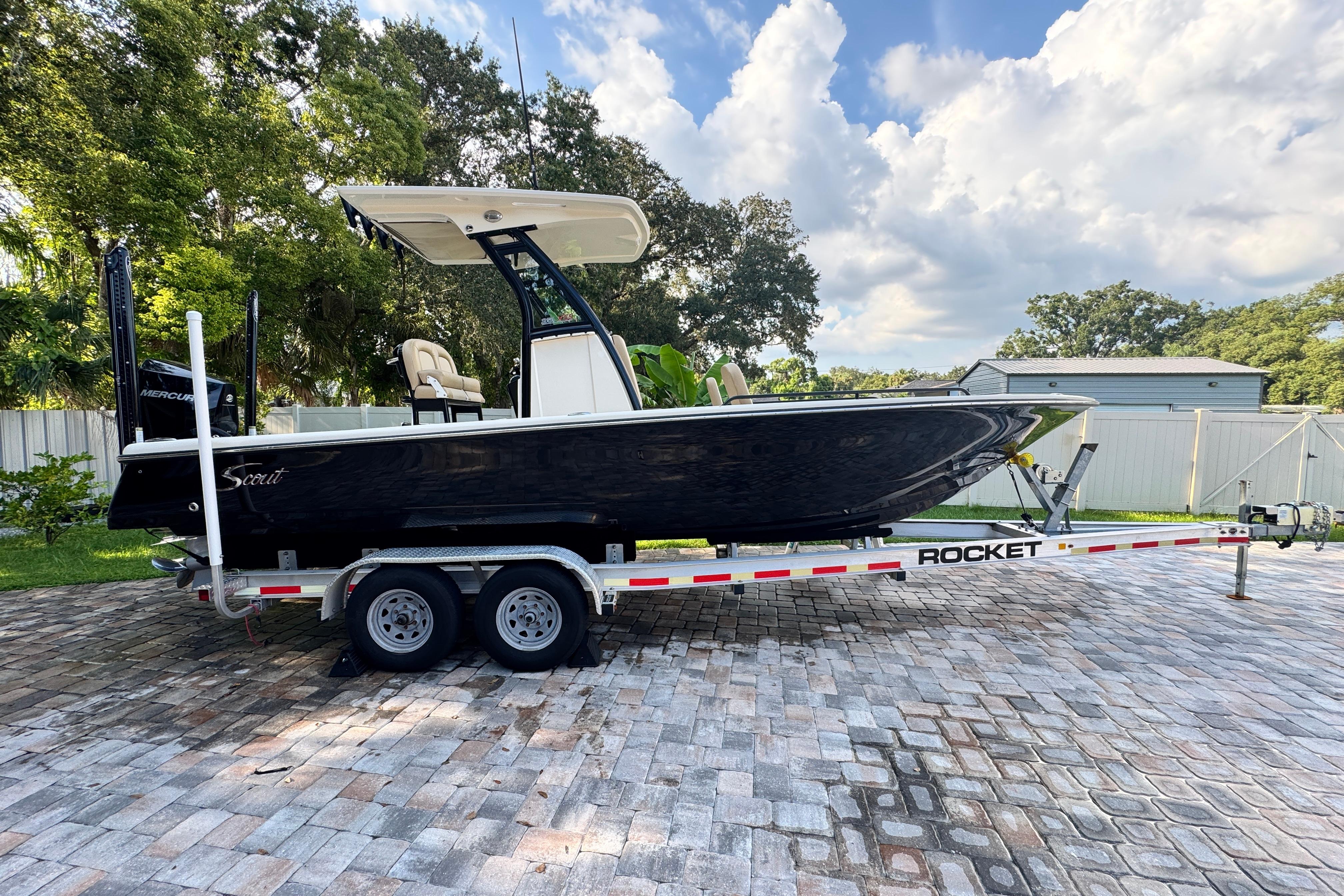 Scout 251 XSS 2020 Scout 251 XSS boat on trailer, parked on paved driveway, surrounded by trees.