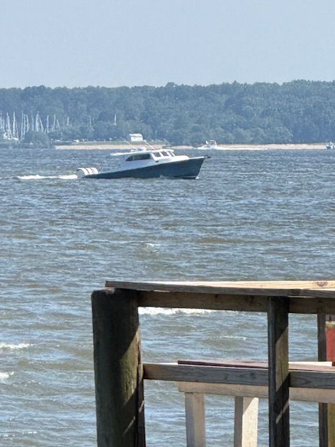 Custom BAYBUILT Custom BAYBUILT 2024 boat cruising on a lake with forested shoreline in the background.
