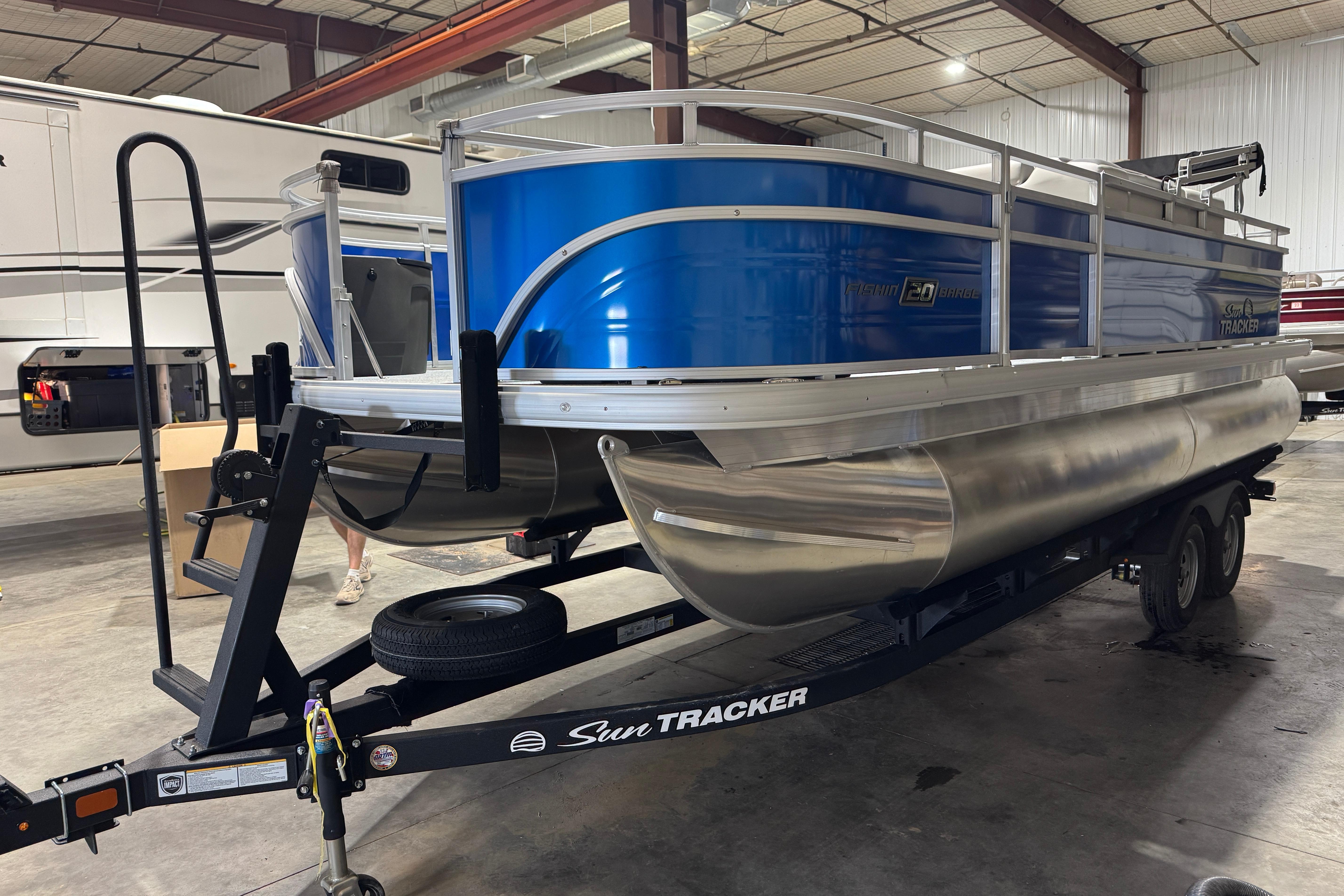 Sun Tracker Fishin' Barge 20 DLX 2026 Sun Tracker Fishin' Barge 20 DLX pontoon boat on trailer in warehouse.