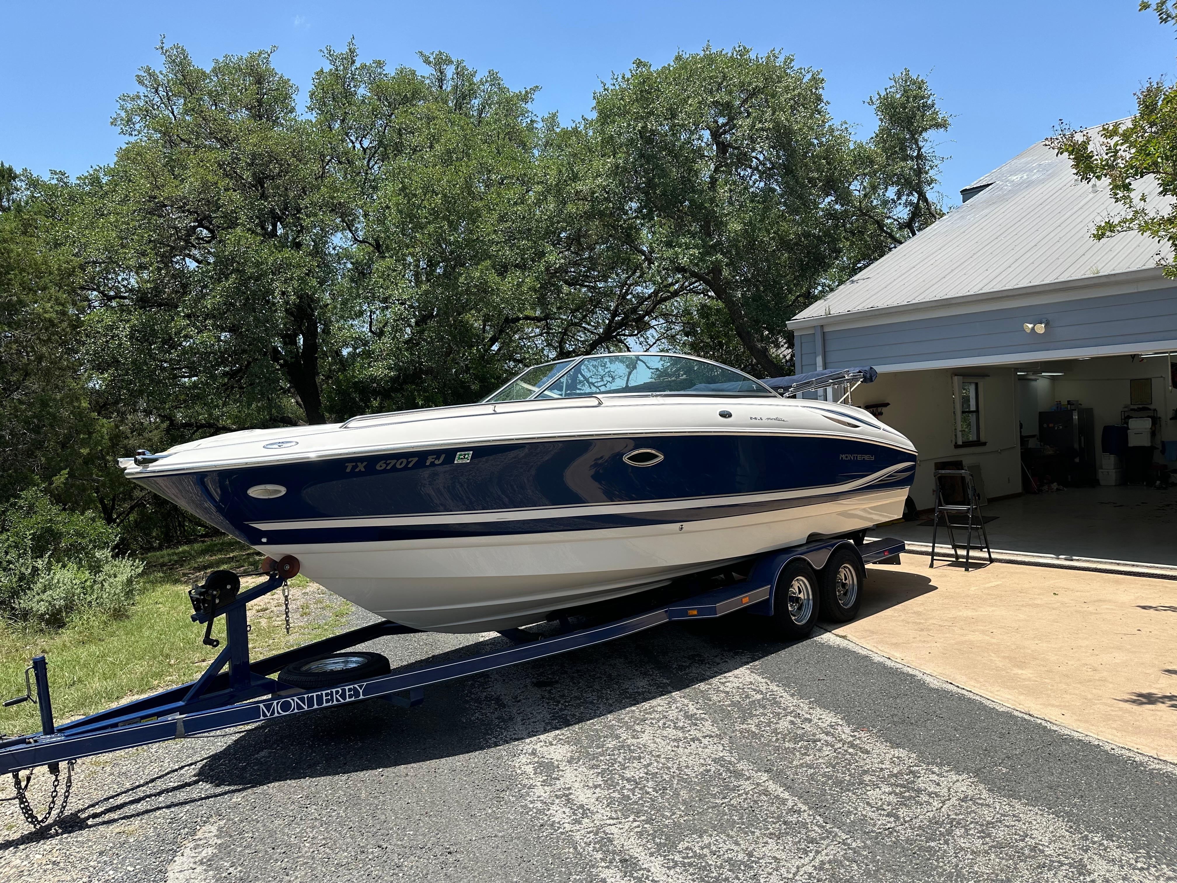 Monterey 248LS Montura 2001 Monterey 248LS Montura boat on trailer, parked near a garage, surrounded by trees.