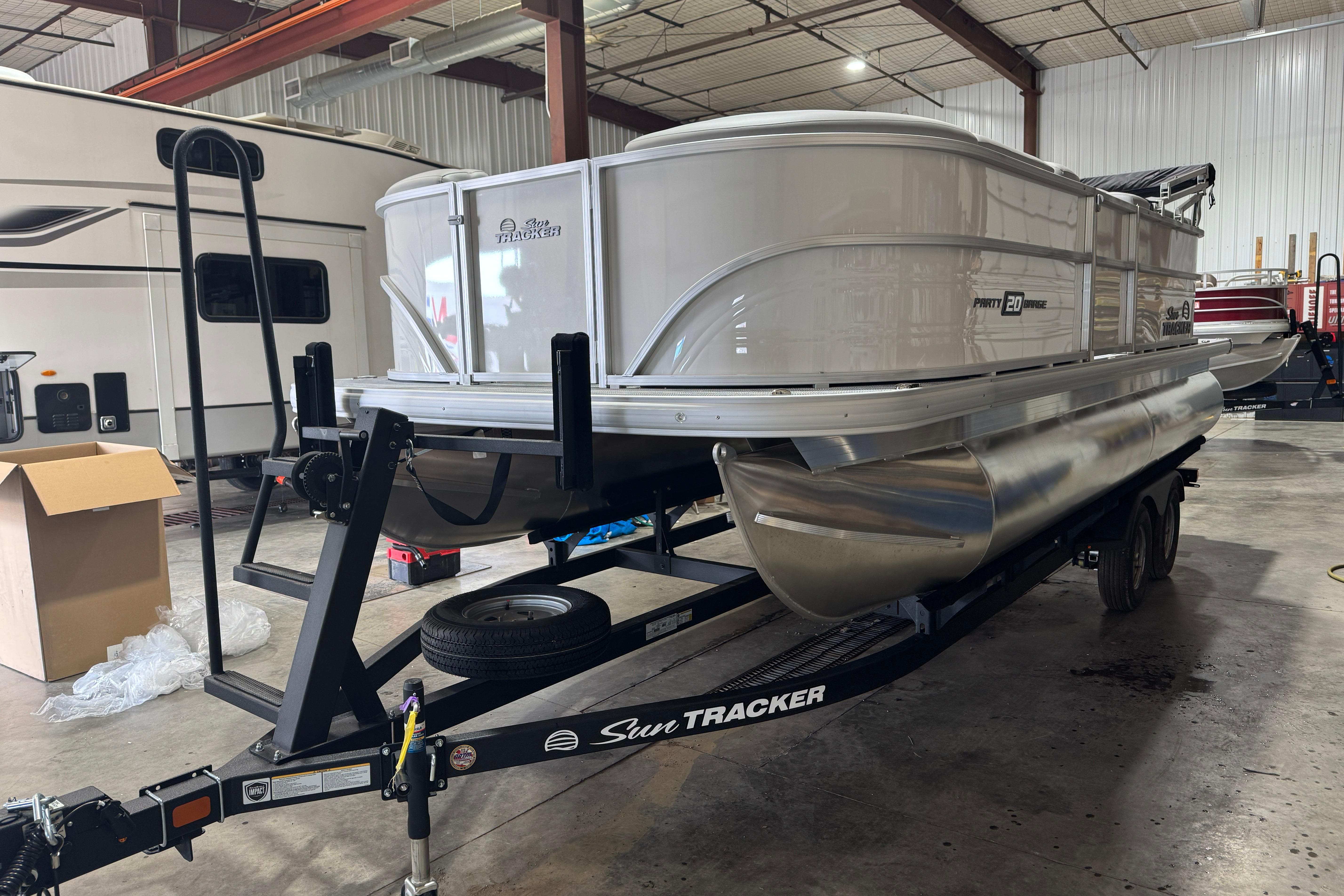 Sun Tracker Party Barge 20 DLX 2026 Sun Tracker Party Barge 20 DLX pontoon boat on trailer in warehouse.