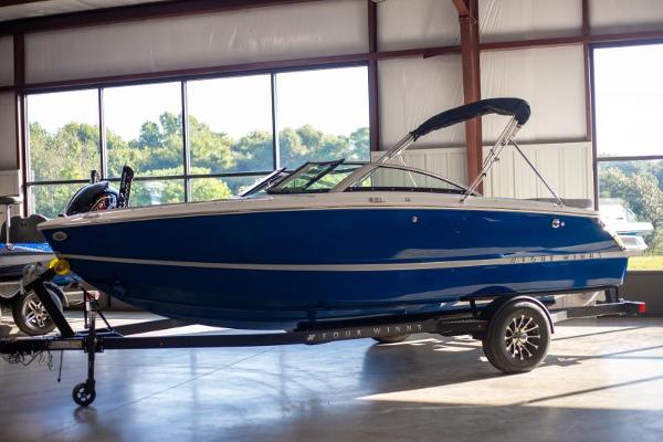 Four Winns H1 2025 Four Winns H1 boat in a showroom, blue exterior, on a trailer.